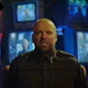 In a scene from found-footage horror film V/H/S/94, a terrified man sits facing the camera in front of several stacked TVs.
